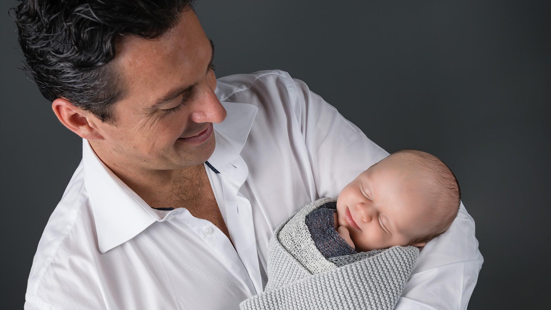 Dad holding baby wrapped in Sydney photography studio on grey background