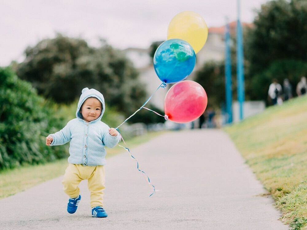 Toddler boy holding balloons in park