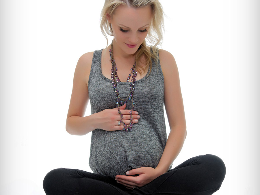Pregnant blonde woman sitting cross legged looking at belly
