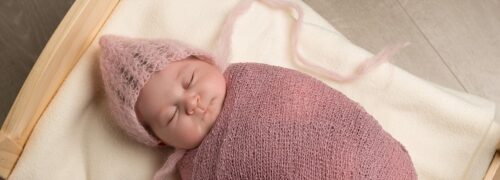 Newborn baby girl in pink wrap and bonnet in bed