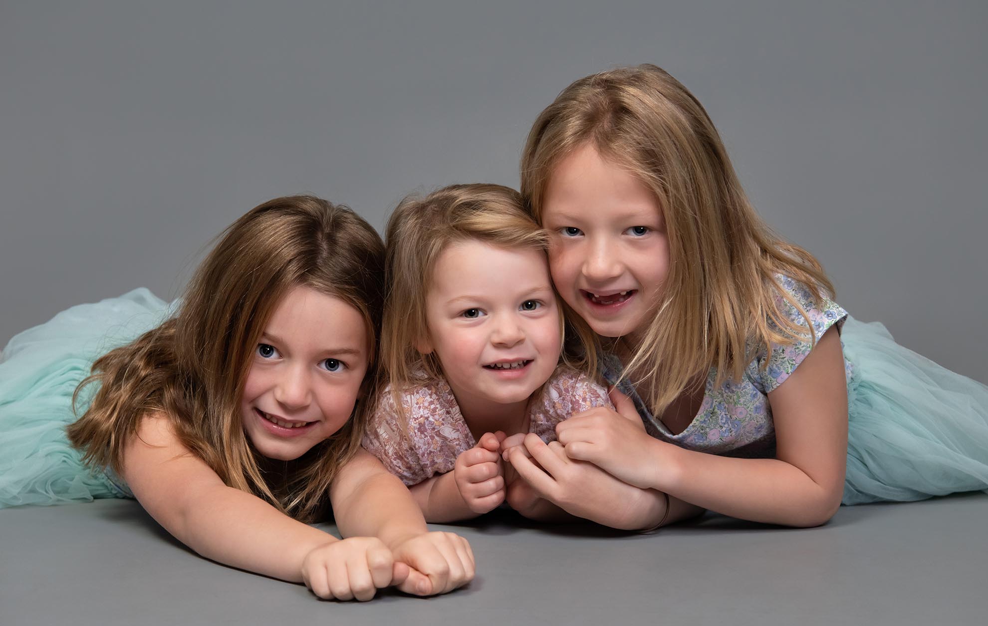 Three young sisters on floor of studio hugging and smiling