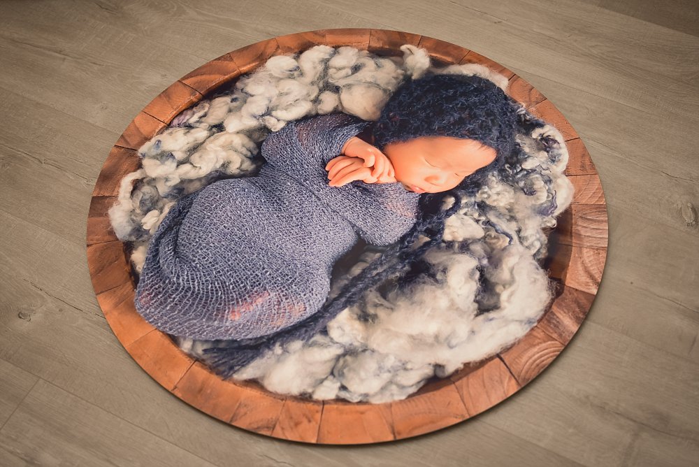 Circular metal artwork of baby in blue wrap and bonnet in bucket