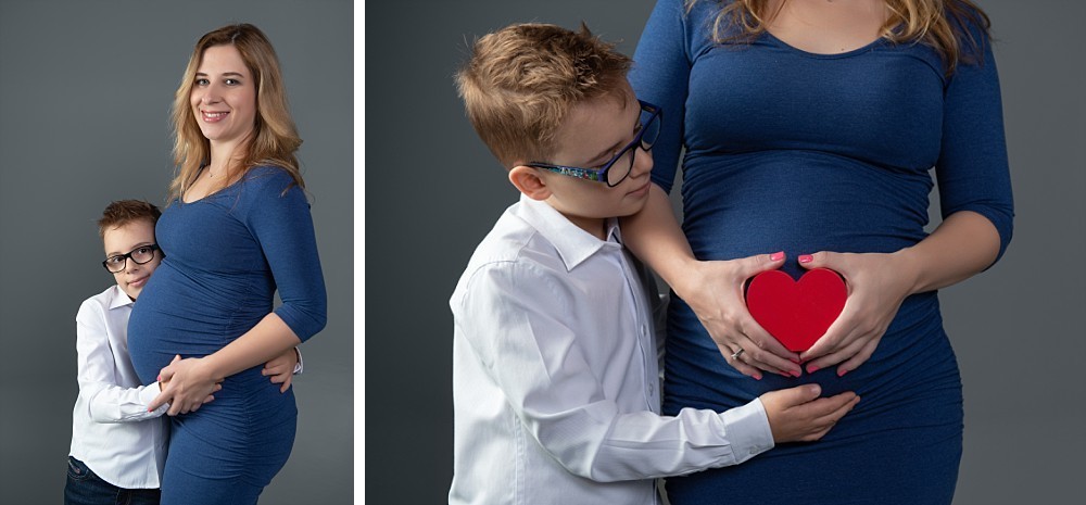 Young boy with glasses listening to belly, pregnant woman in blue dress in Sydney studio